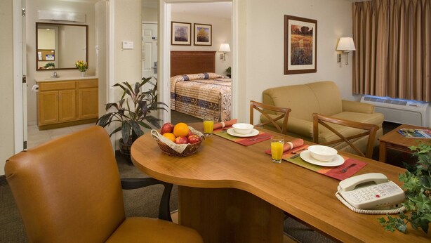 Une chambre d’hôtel avec une table à manger en bois, un téléphone, un panier de fruits et un lit doté d’une tête de lit.