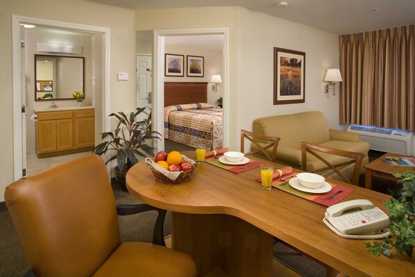 Une chambre d’hôtel avec une table à manger en bois, un téléphone, un panier de fruits et un lit doté d’une tête de lit.