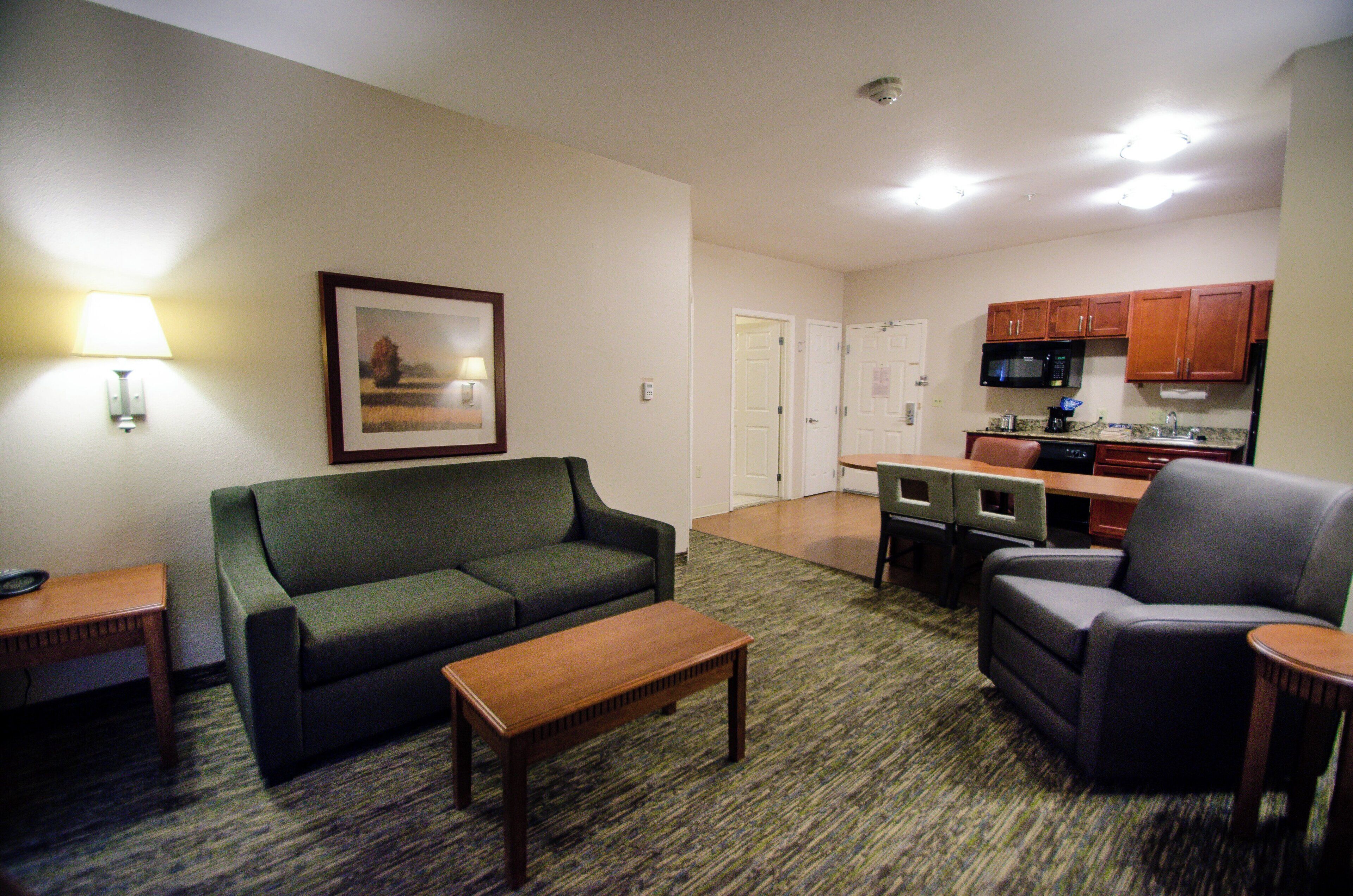 A living room with a sofa, a chair, a coffee table, and a kitchen area with a microwave and cabinets.