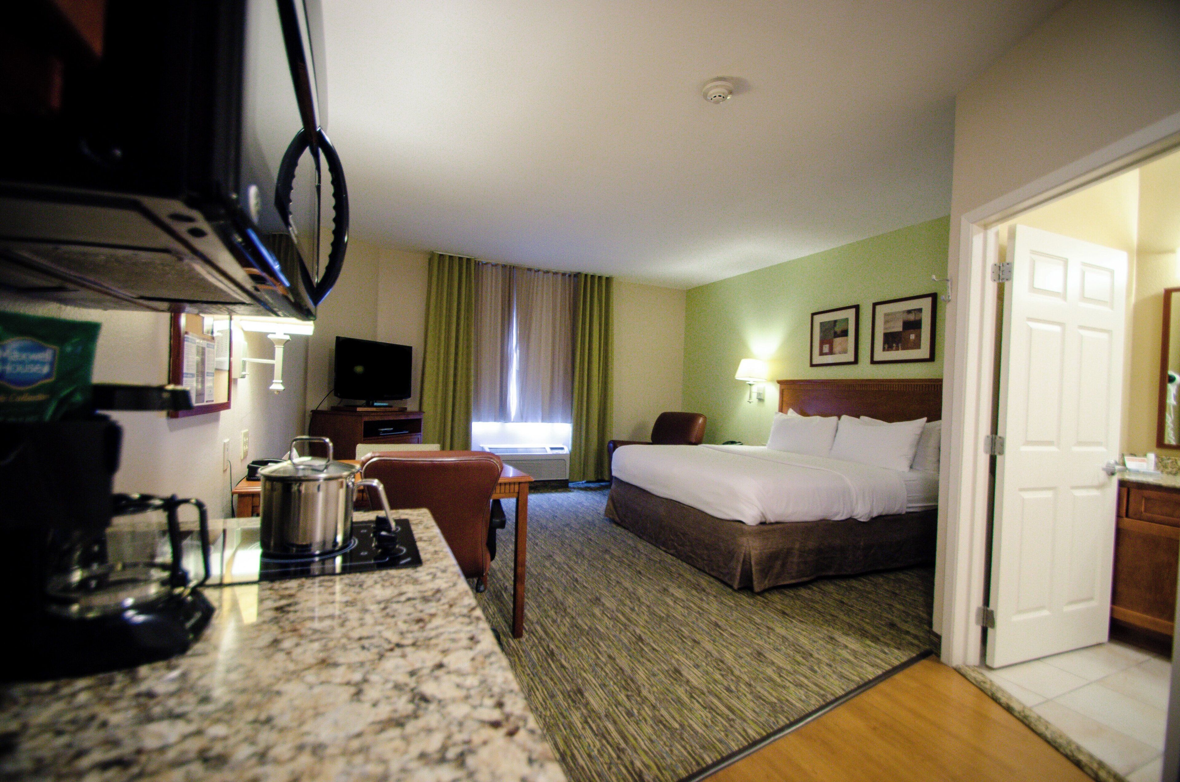 A hotel room with a bed, a desk with a kettle, a television, and a window with curtains.
