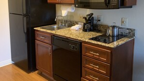 Une cuisine compacte avec des meubles en bois, un réfrigérateur noir, un four à micro-ondes en acier inoxydable et un lave-vaisselle.