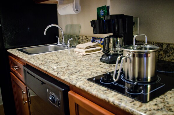 Una cocina con encimeras de granito, lavavajillas, cafetera y una olla en la estufa.