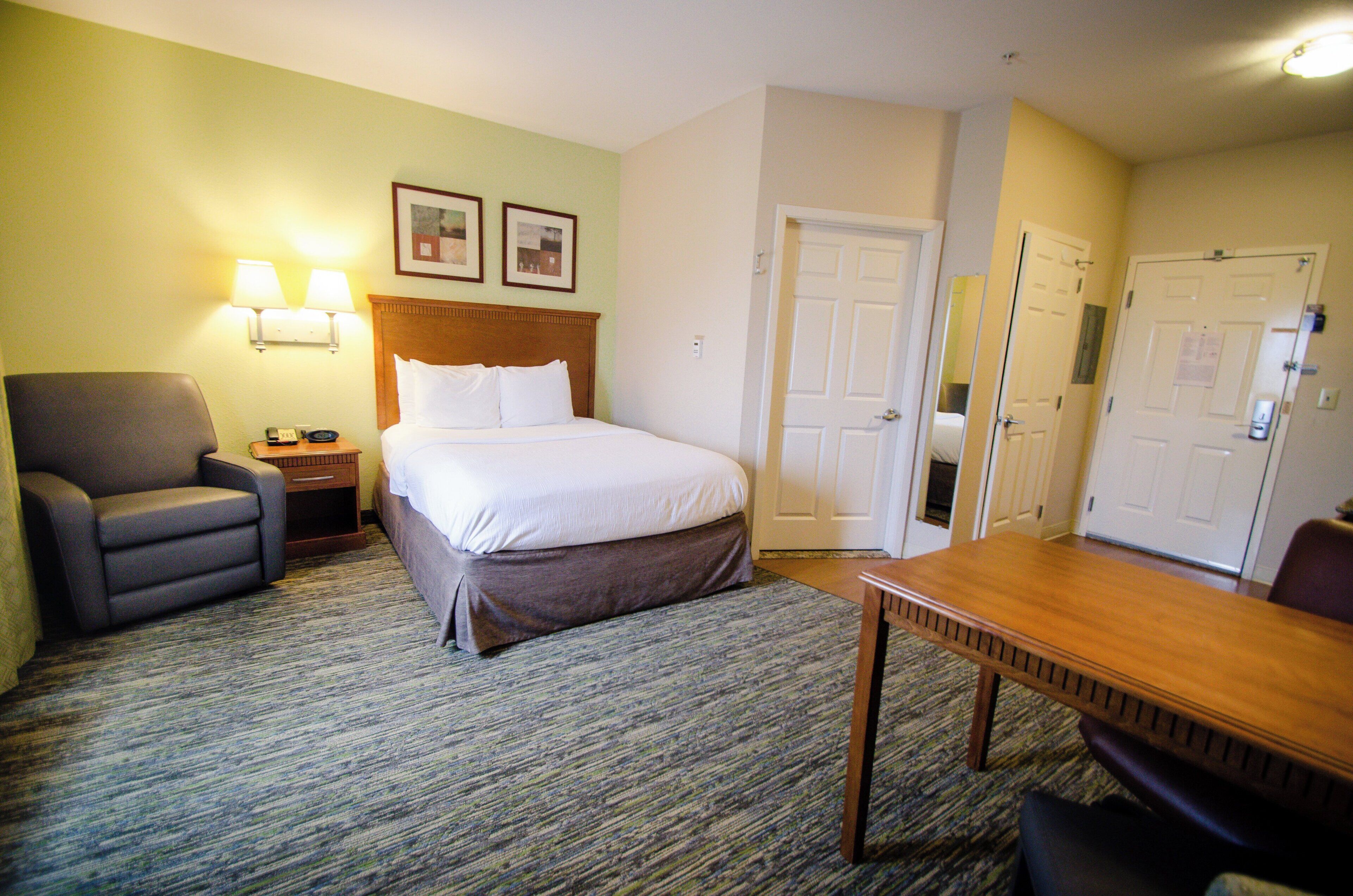 A hotel room with a bed, a chair, a table, and two doors.