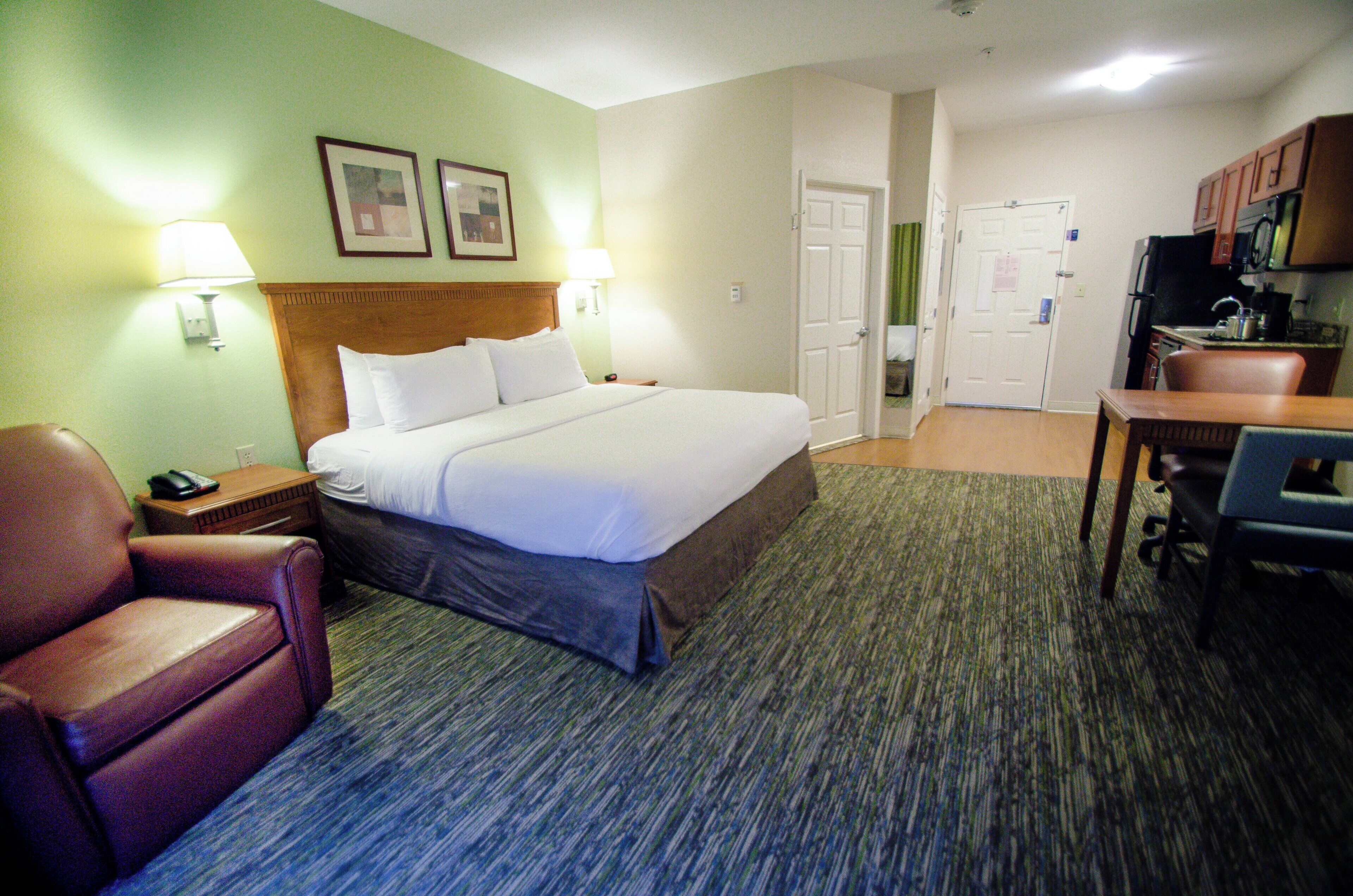 A hotel room with a bed, a chair, a desk, and a kitchenette.