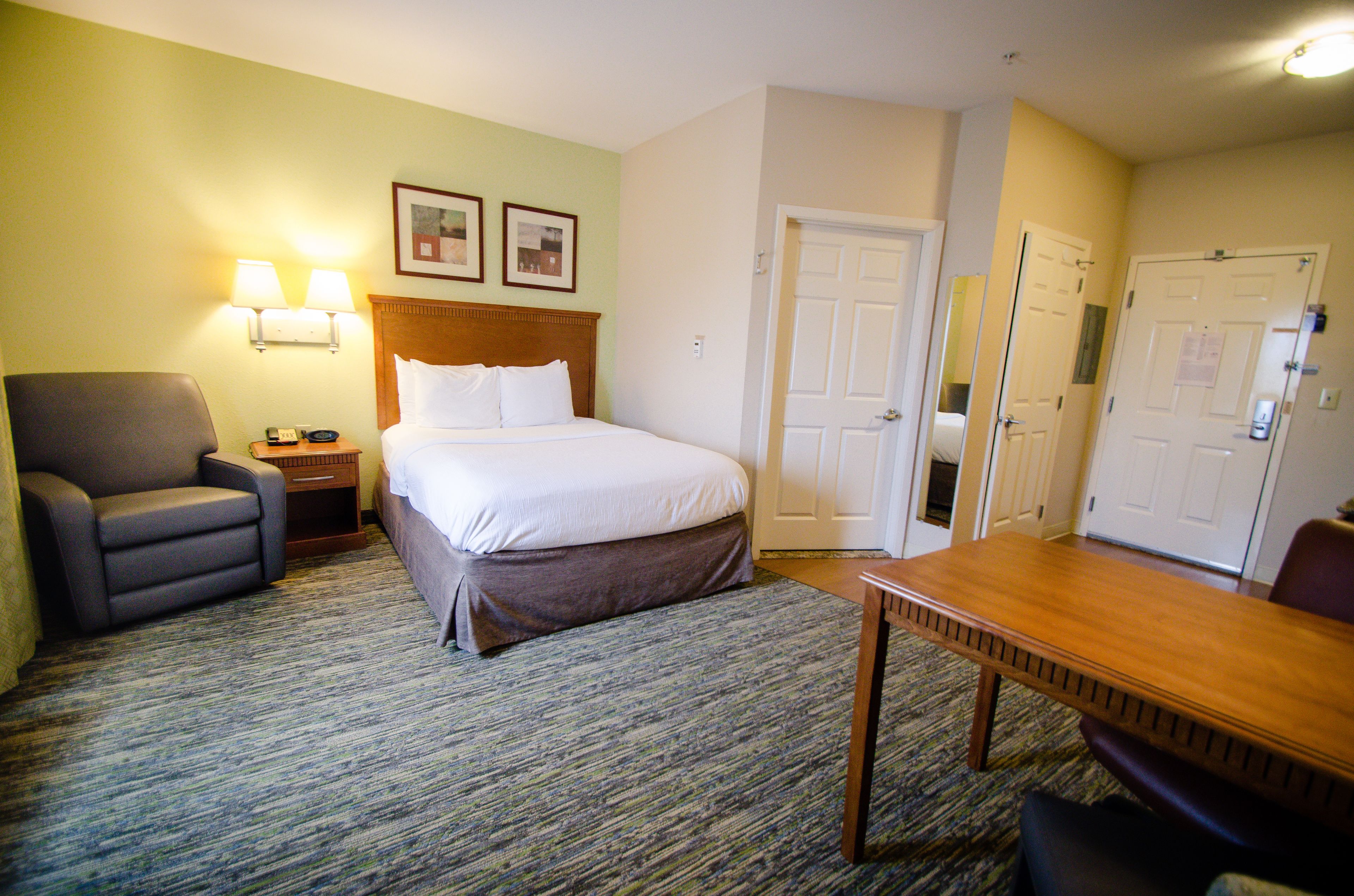 Une chambre d’hôtel avec un lit, un bureau, une chaise, une lampe et une porte.