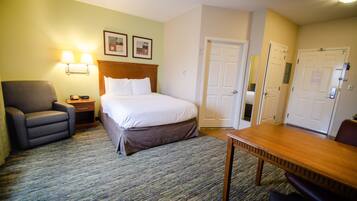 Une chambre d’hôtel avec un lit, un bureau, une chaise, une lampe et une porte.