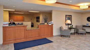 A reception area with a wooden desk, two patterned chairs, a blue rug, and a clock on the wall.