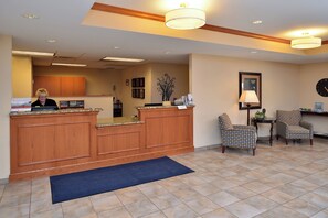 A reception area with a wooden desk, two patterned chairs, a blue rug, and a clock on the wall.
