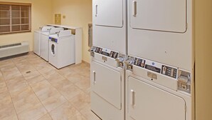 A laundry room with a front-loading washer and dryer, a vented heater, and a control panel with various buttons and indicators. - Candlewood Suites Williston by IHG (Williston)