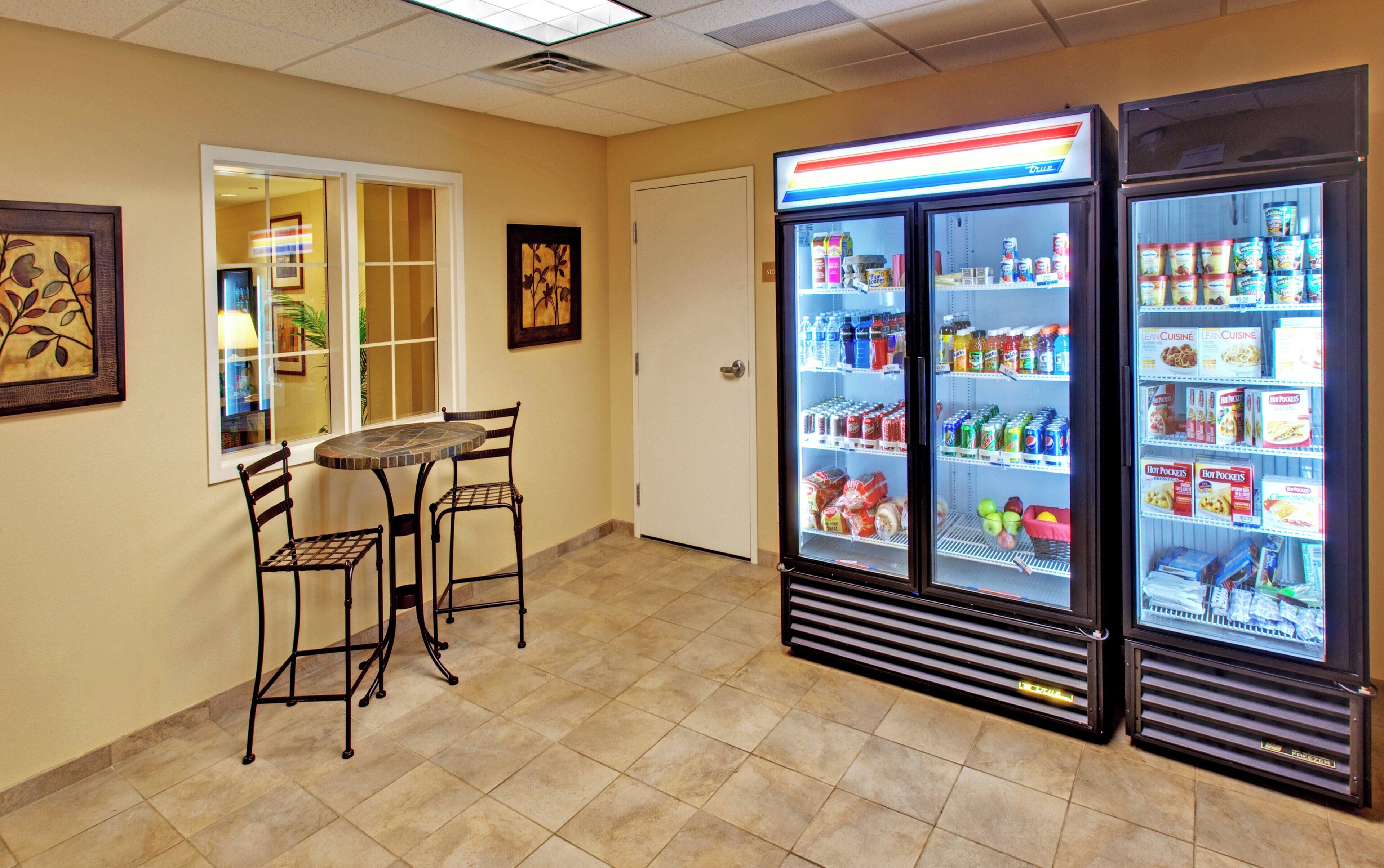 A room with a table and chairs, a refrigerator stocked with beverages, and a door leading to another room.