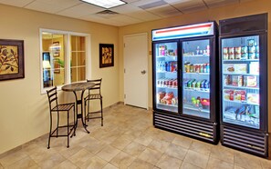 A room with a table and chairs, a refrigerator stocked with beverages, and a door leading to another room. - Candlewood Suites Williston by IHG (Williston)