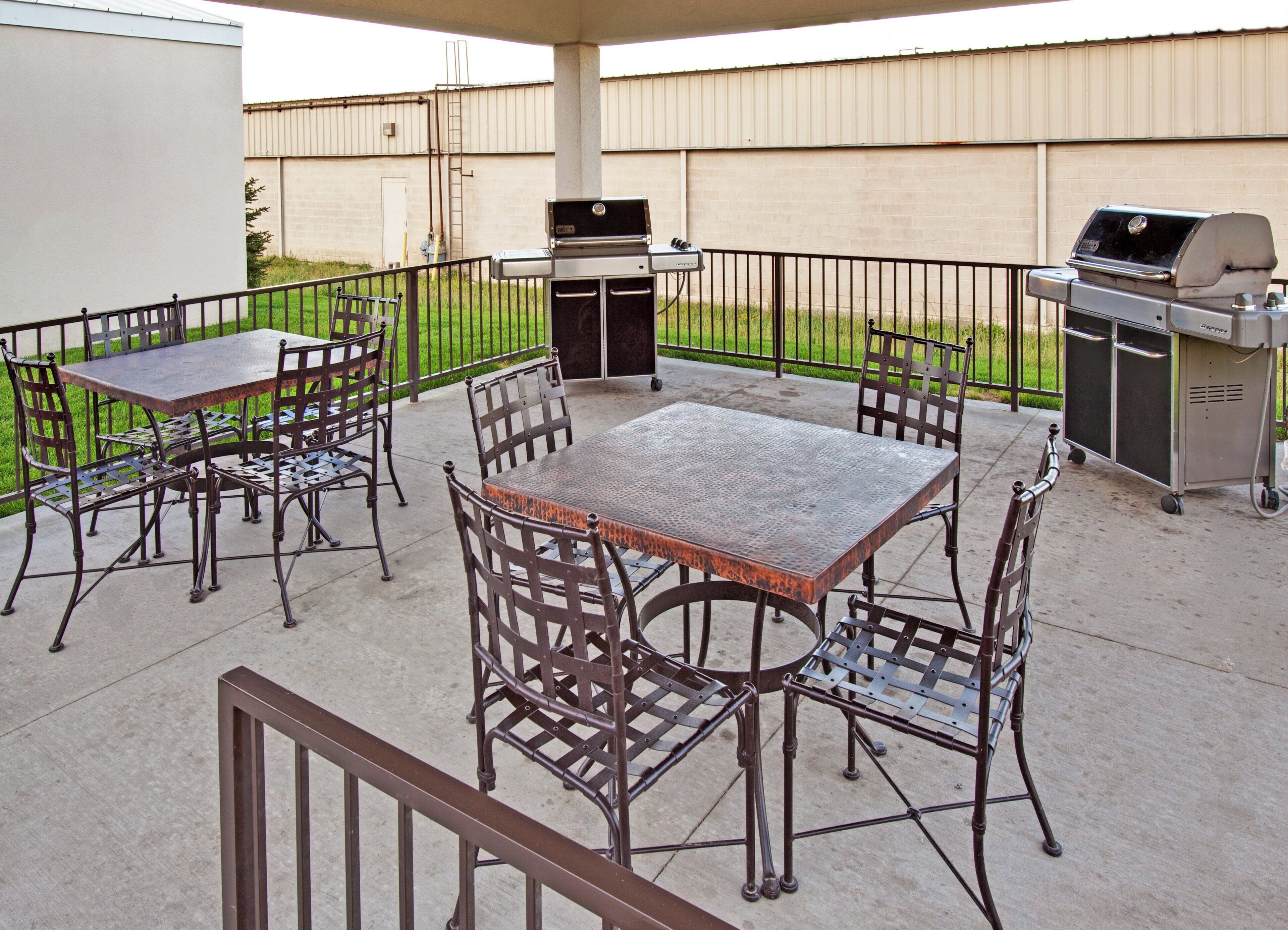 Un patio exterior con una mesa y sillas de metal, una parrilla y un carrito.