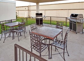 An outdoor patio with a metal table and chairs, a barbecue grill, and a cart. - Candlewood Suites Williston by IHG (Williston)