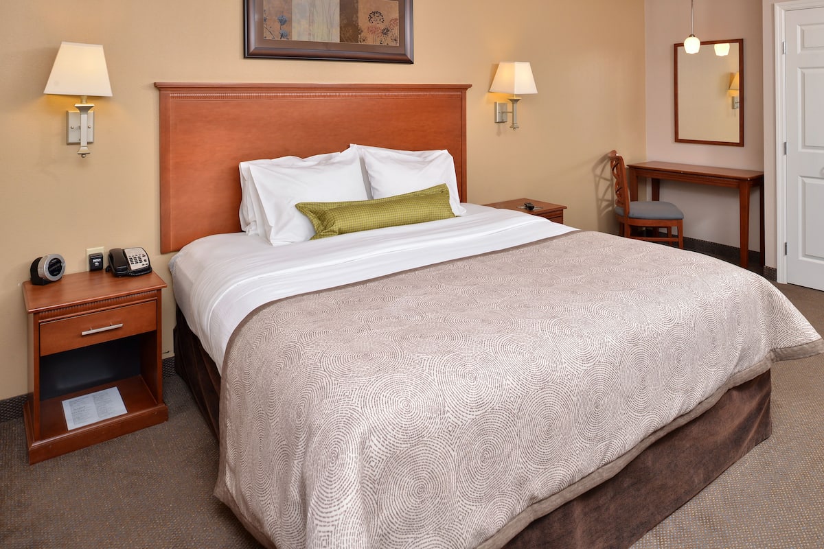 A hotel room with a large bed, two bedside tables, a desk, and a chair.