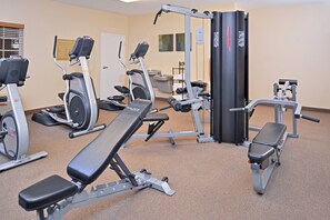Un gimnasio con diversos equipos de ejercicio, incluyendo cintas de correr, elípticas y máquinas de pesas.