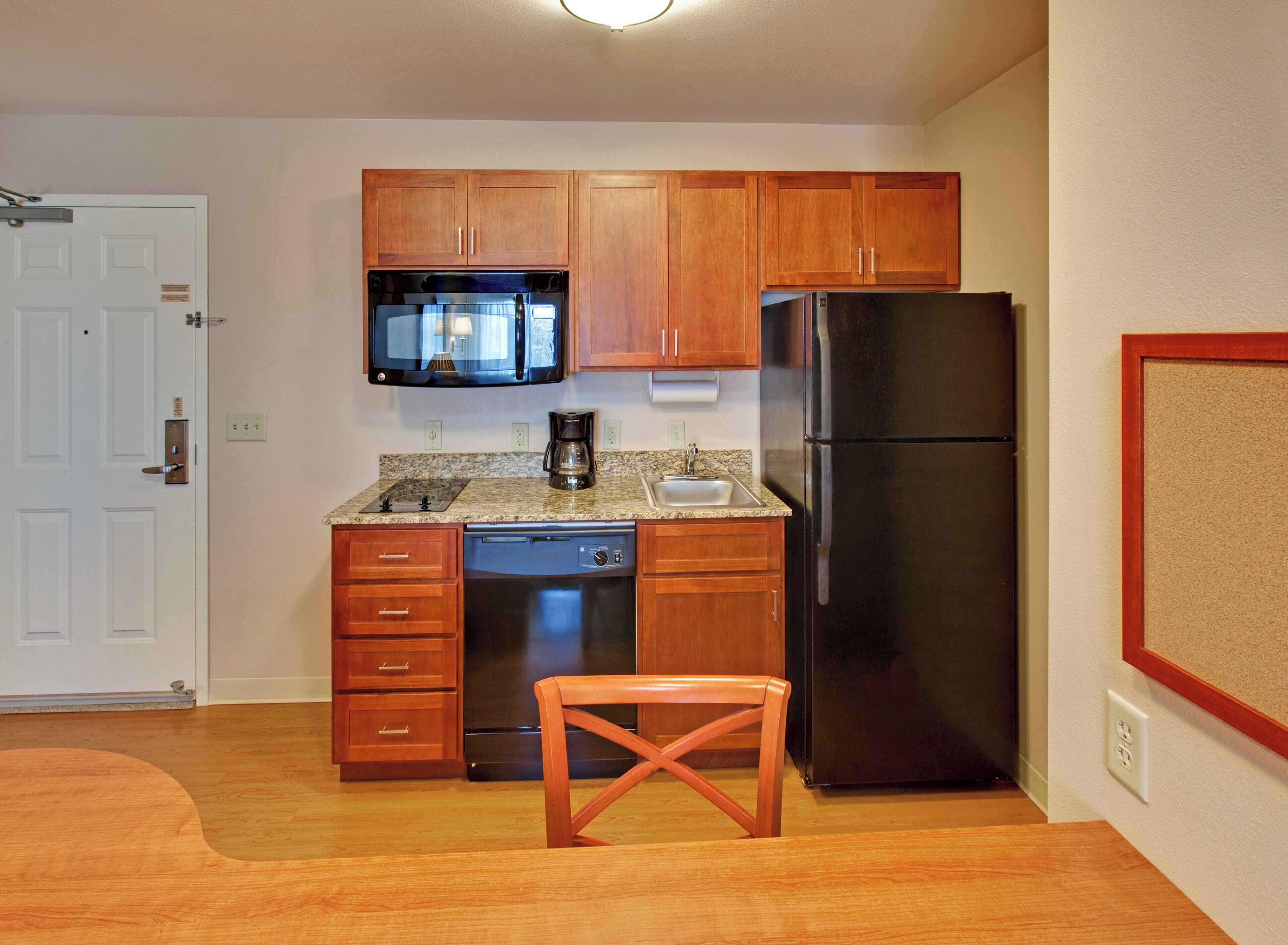 Una cocina compacta con armarios de madera, un refrigerador de acero inoxidable, un microondas y una cafetera.