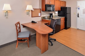 A compact kitchen with a microwave, refrigerator, and a small dining area with a chair and table. - Candlewood Suites Williston by IHG (Williston)