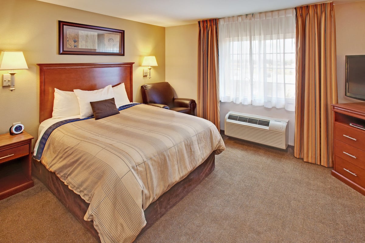 A hotel room with a large bed, two bedside lamps, a chair, a TV, and a window with curtains.