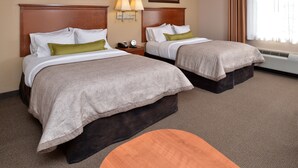 A hotel room with two beds, a nightstand with a lamp, a small table, and a window with curtains. - Candlewood Suites Williston by IHG (Williston)