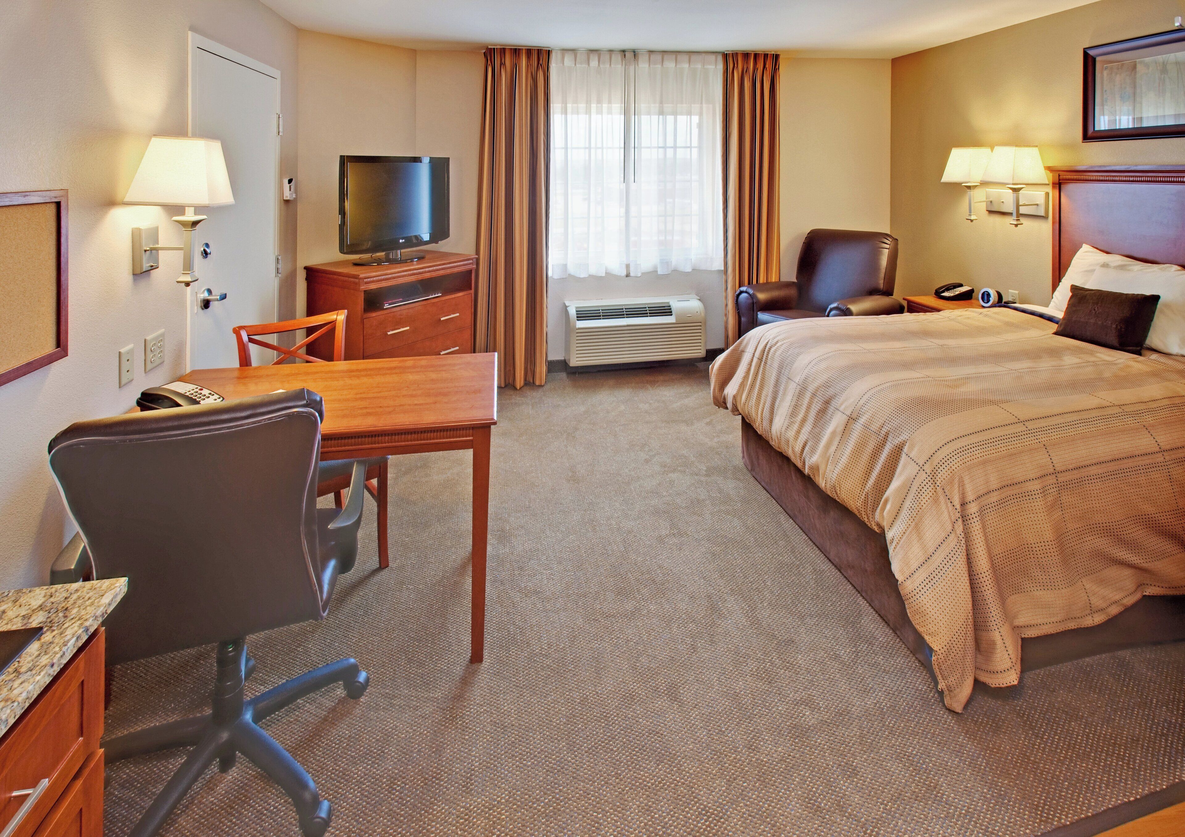 Habitación de hotel con cama, escritorio, silla, televisor, aire acondicionado y lámparas.