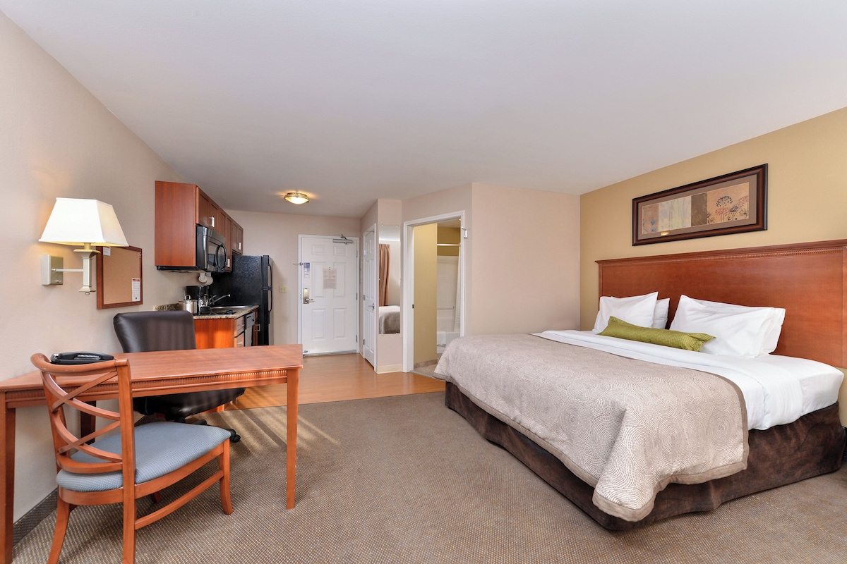 A hotel room with a bed, a desk, a chair, a microwave, and a door leading to a bathroom.