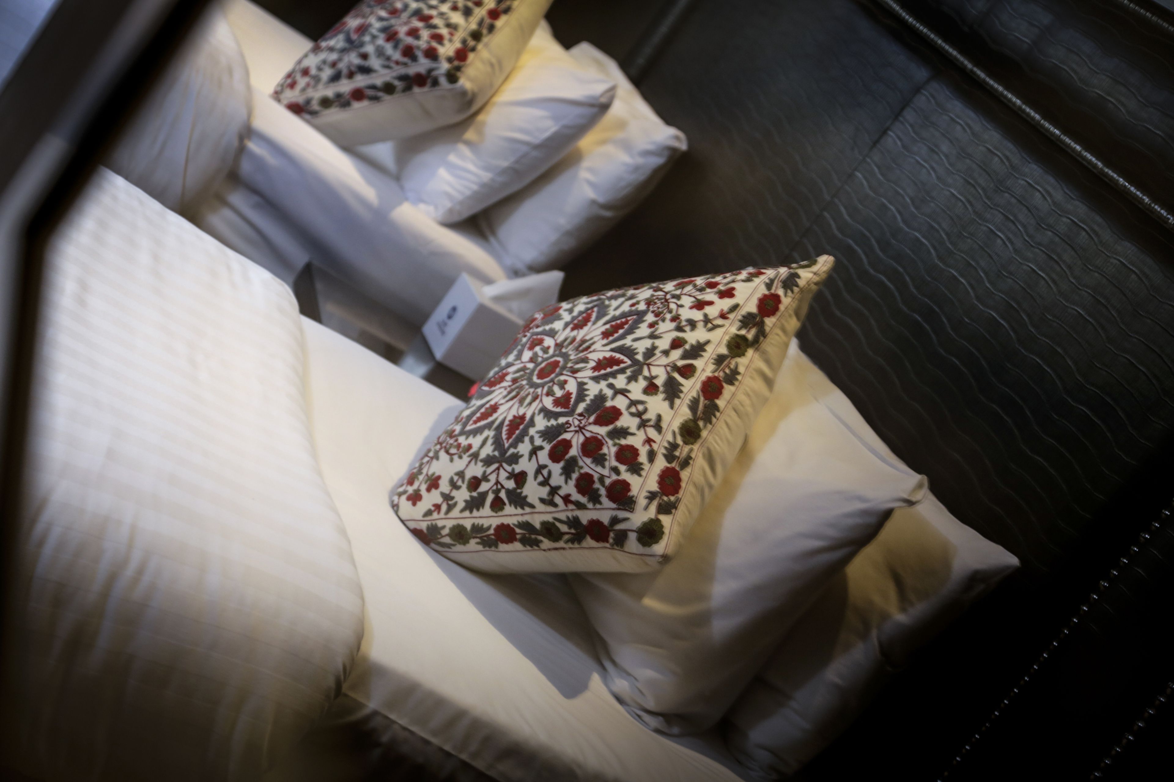 Habitación de hotel con cabecera oscura, ropa de cama blanca y almohadas decorativas con motivos florales.