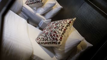 Habitación de hotel con cabecera oscura, ropa de cama blanca y almohadas decorativas con motivos florales.