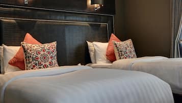 Une chambre d’hôtel avec une tête de lit sombre, deux lits avec du linge de lit blanc et des coussins décoratifs.