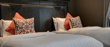 A hotel room with a dark headboard, two beds with white linens, and decorative pillows.