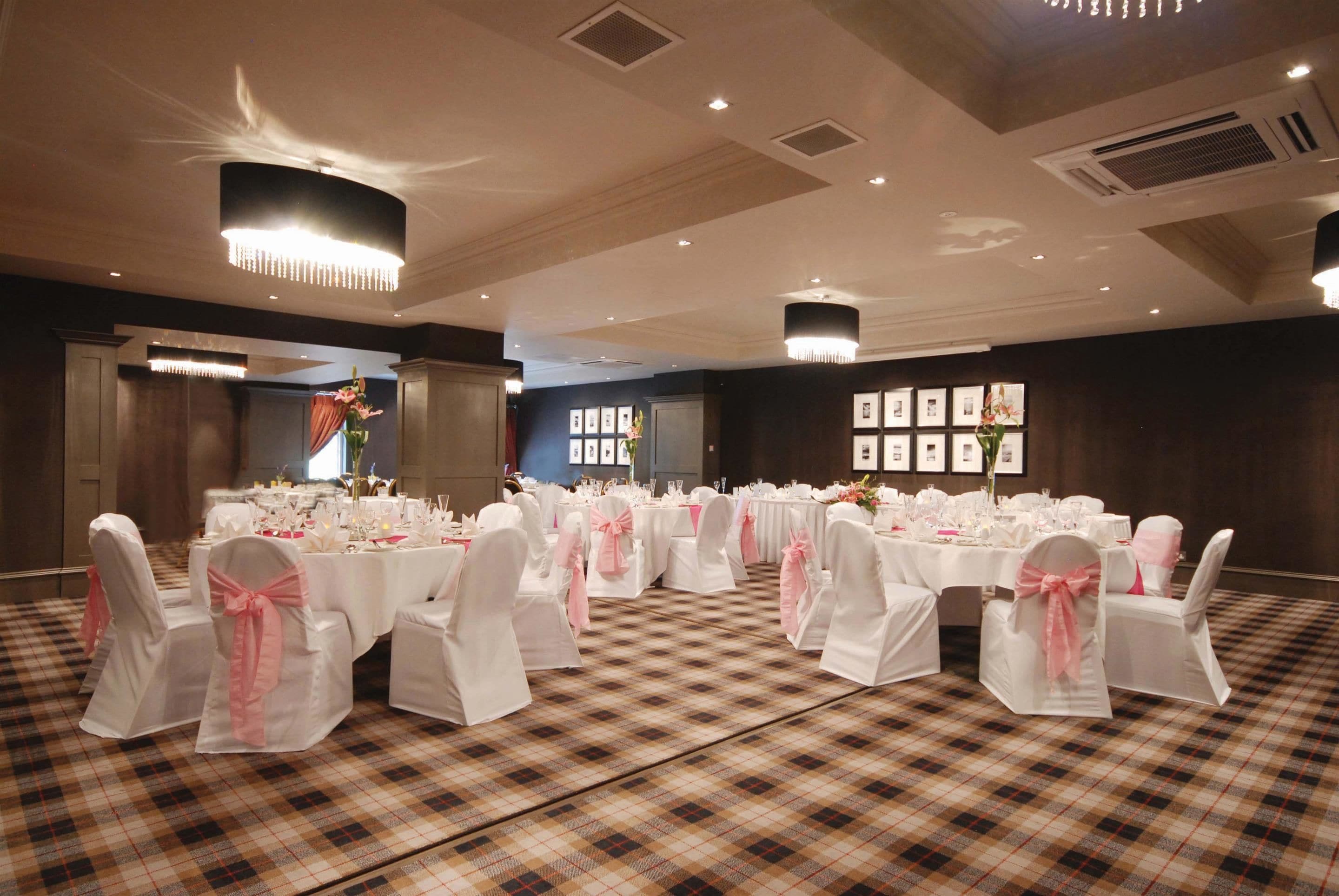 A banquet hall with round tables set for a formal event, featuring white tablecloths and pink chair covers.