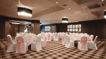 A banquet hall with round tables set for a formal event, featuring white tablecloths and pink chair covers.