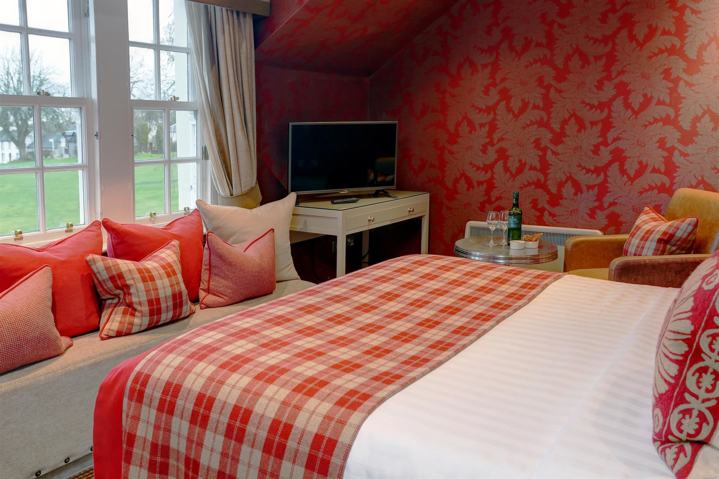 Habitación de hotel con una cama grande, un televisor sobre una mesita y vistas al exterior a través de una ventana.