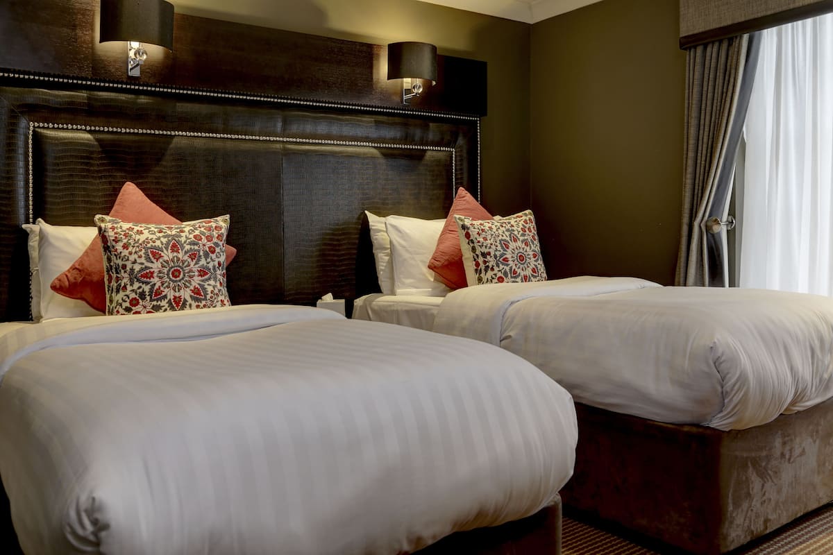 A hotel room with two beds, a dark headboard, and a window with curtains.