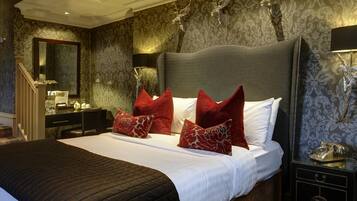 Habitación de hotel con una cama grande, almohadas rojas, una mesita de noche con lámpara, un espejo y un aparador.