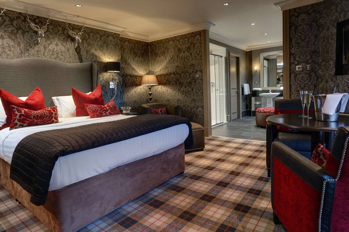 A hotel room with a large bed, a nightstand, a chair, and a table with a lamp.
