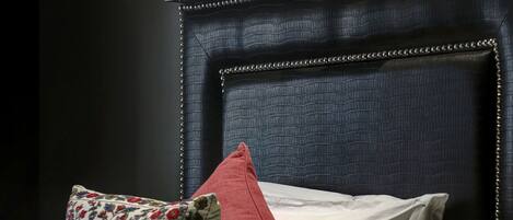 A neatly made bed with white and red pillows, a dark headboard, and a wall-mounted lamp.