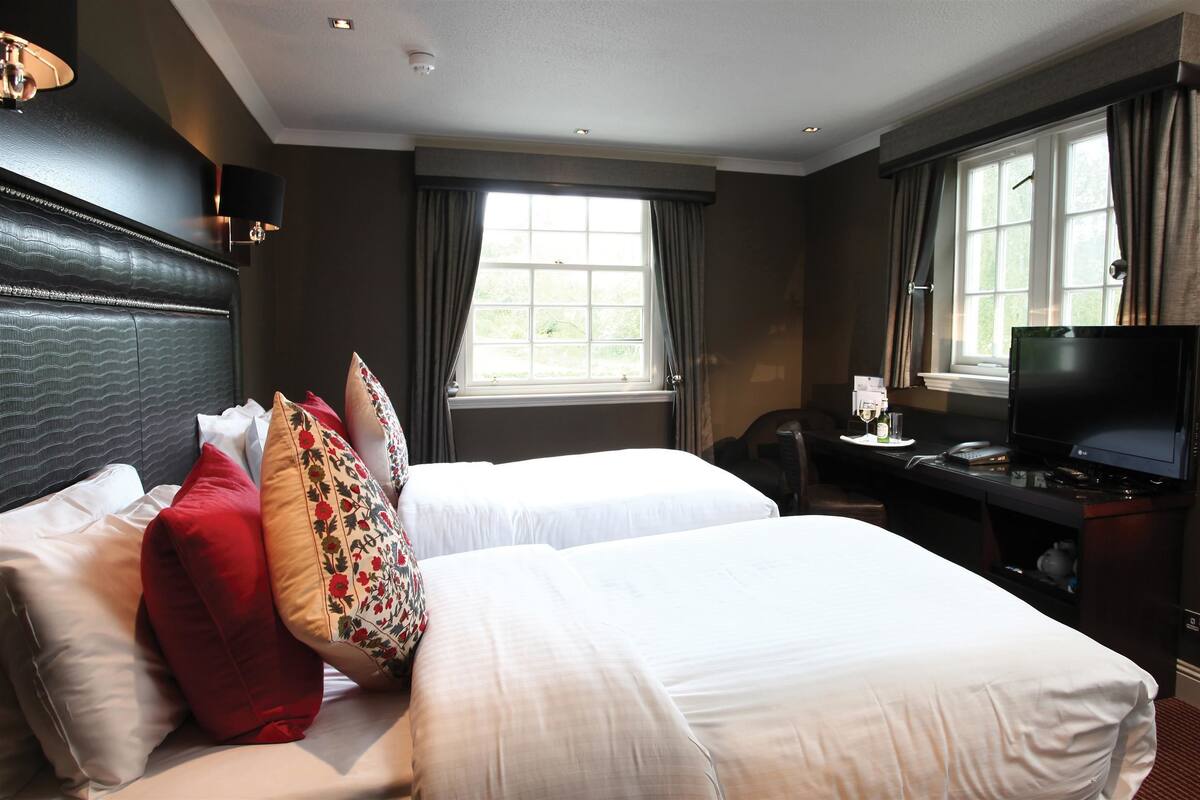 A hotel room with two beds, a desk with a TV, and a window with curtains.