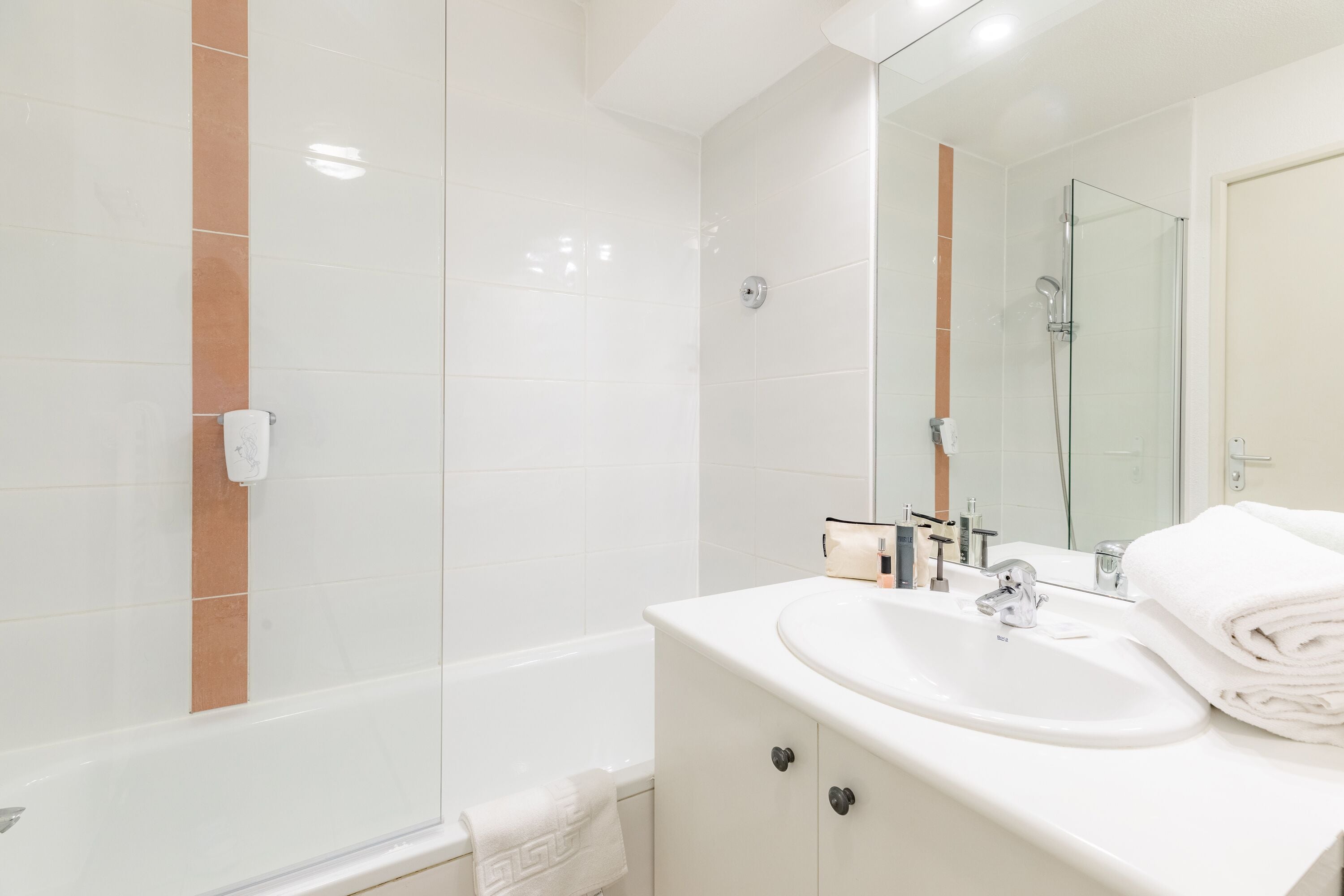 Un baño moderno con cabina de ducha de vidrio, un lavabo blanco con espejo y un perchero para toallas.