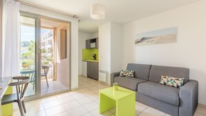 A modern living room with a grey sofa, a green coffee table, and a dining area with a table and chairs. - Appart'City Confort La Ciotat Cote Port (La Ciotat)