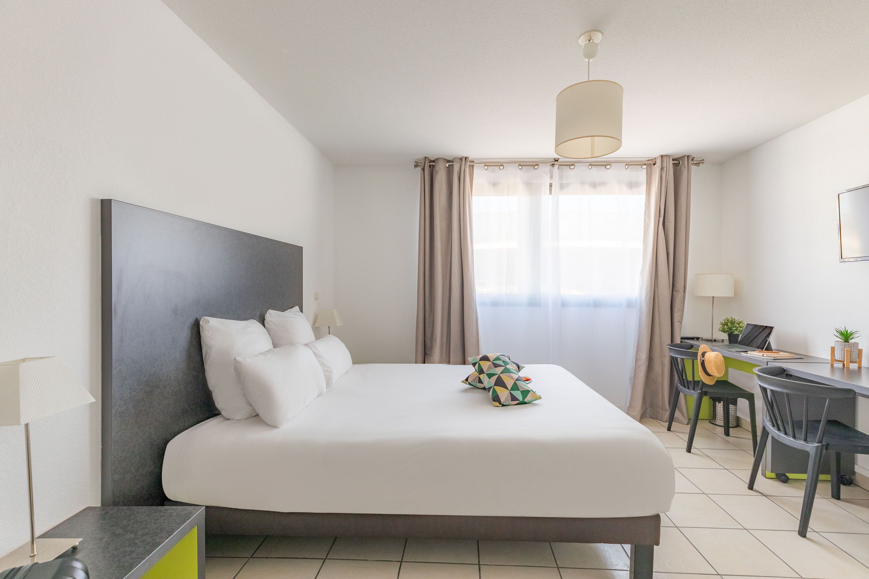 A modern hotel room with a large bed, a desk, and a chair.