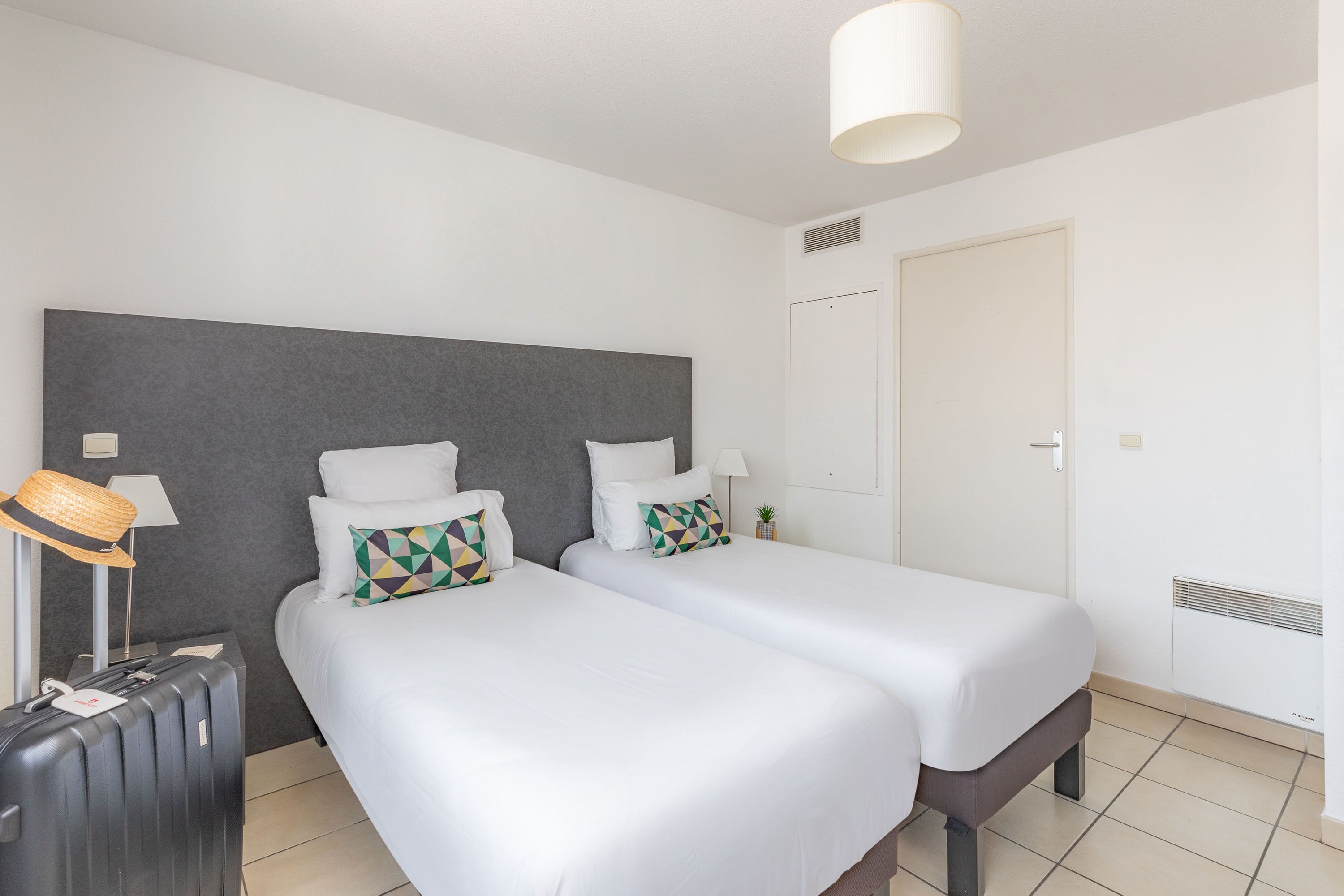 A hotel room with two beds, a suitcase, a lamp, and a door.