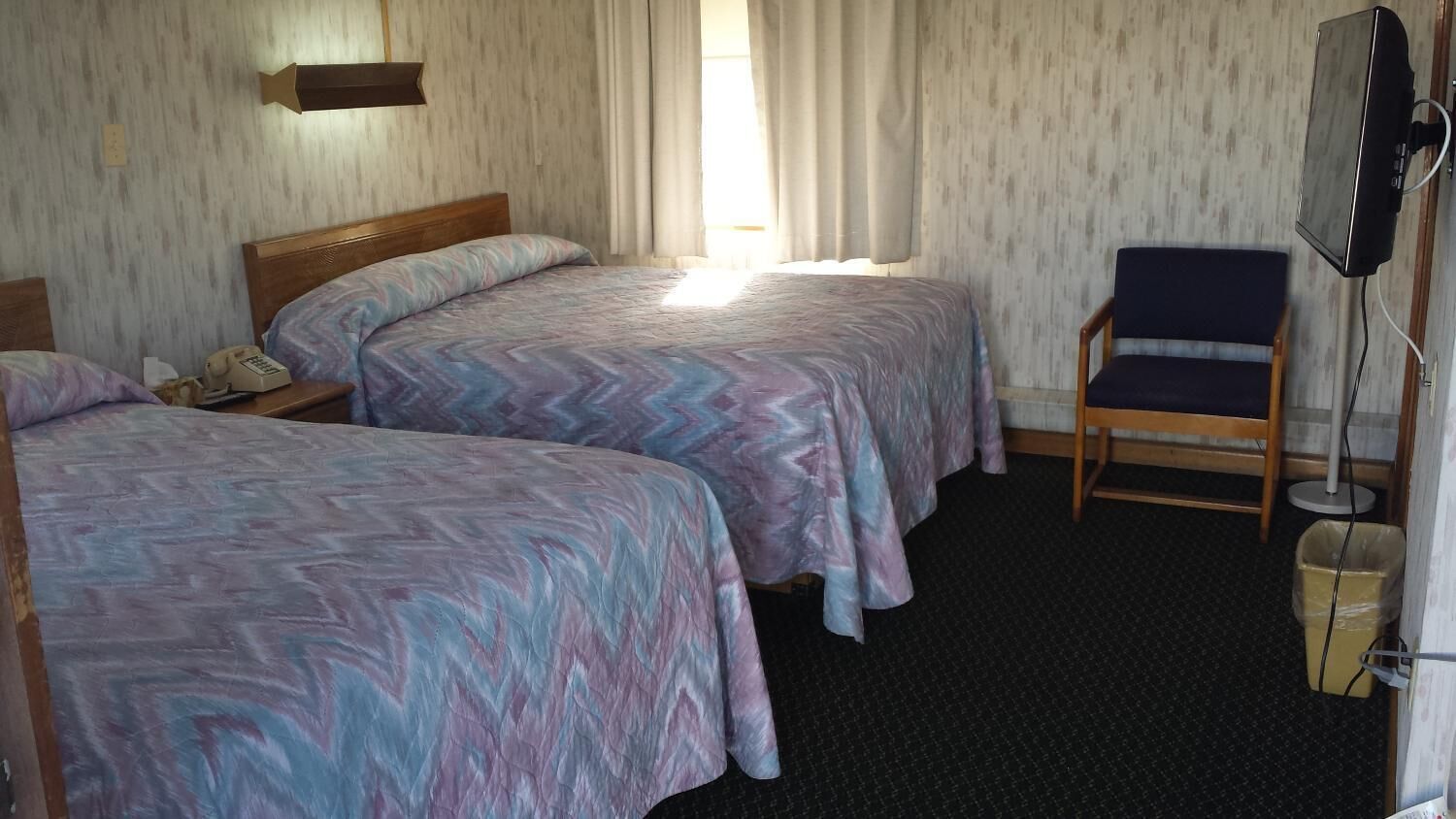 Habitación de hotel con dos camas, una silla, un televisor y un cubo de basura.