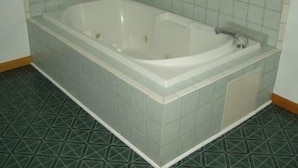 Uma banheira retangular padrão, com uma única torneira, paredes revestidas de azulejos e um ch ão com padrão geométrico.