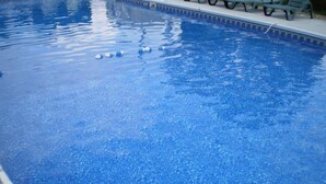 Una piscina blava i nítida amb un voreig trencadís i algunes gandules a la vora.