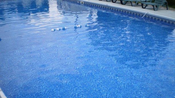 Piscina azul clara com borda azulejada e alguns cadezões ao redor.