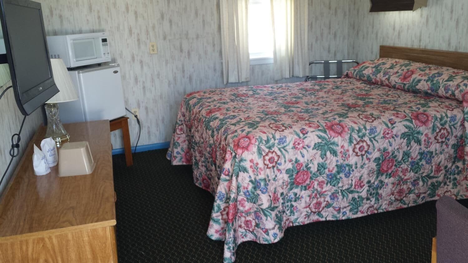 A hotel room with a bed, a desk with a lamp, a microwave, and a small refrigerator.