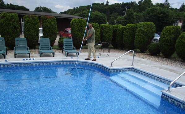 En swimmingpool med flisekant, omgivet af grønne stole og en rød bil i baggrunden.