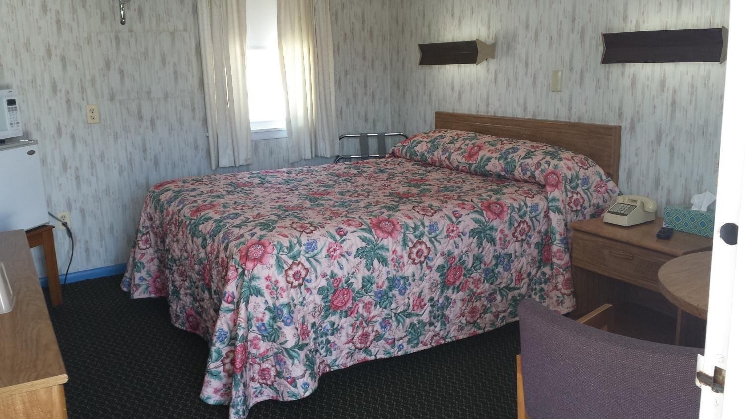 Een hotelkamer met een bed, een bureau, een stoel, een telefoon en een klein tafeltje.