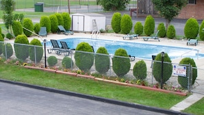Piscina com área cercada, cadeiras de descanso e aviso.