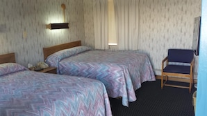 Quarto de hotel com duas camas, uma cadeira e uma mesa de cabeceira com telefone.